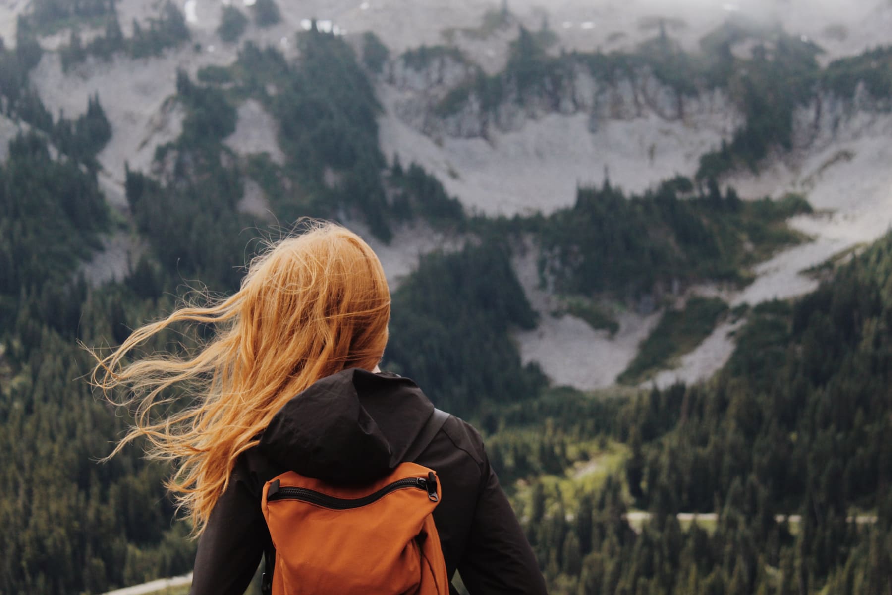 Woman with orange backpack looking over mountains