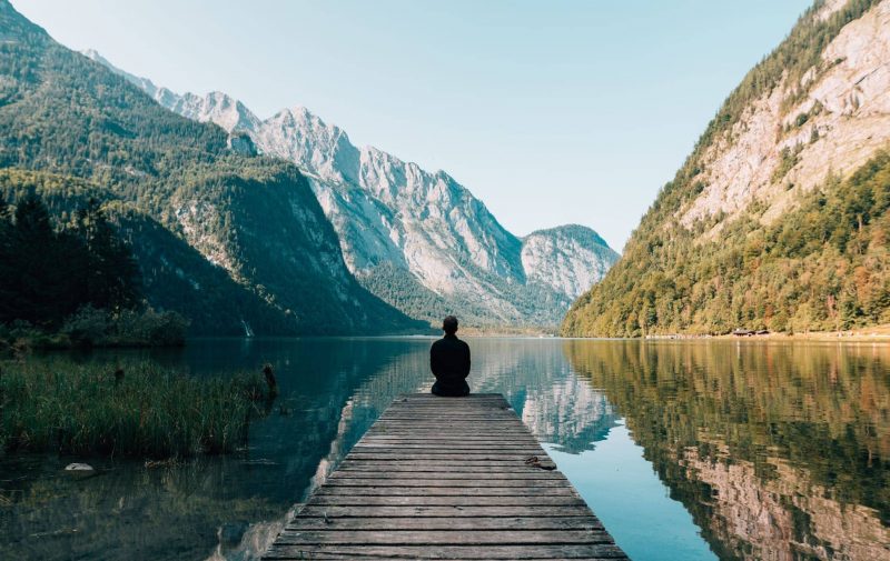 Man sitting on a deck looking out over a lake and mountains