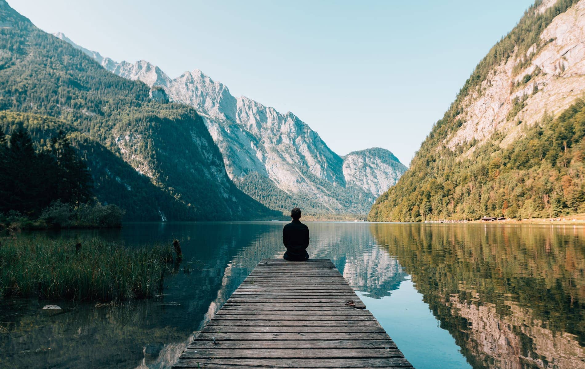 Man sitting on a deck looking out over a lake and mountains