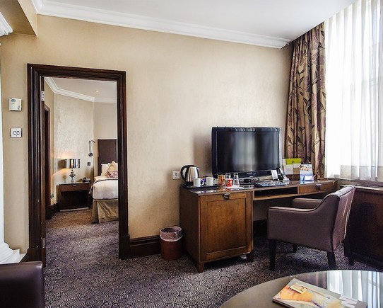 Large bedroom with a desk, chair, tv screen and tea making facilities.