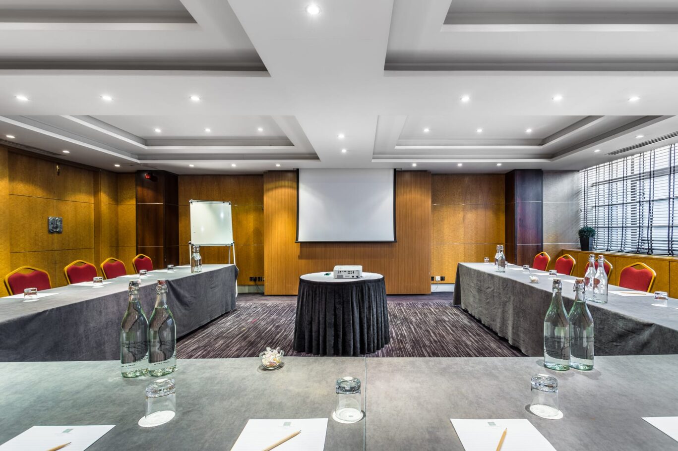 Centre view of the large meeting room with round table in the middle and projector screen.