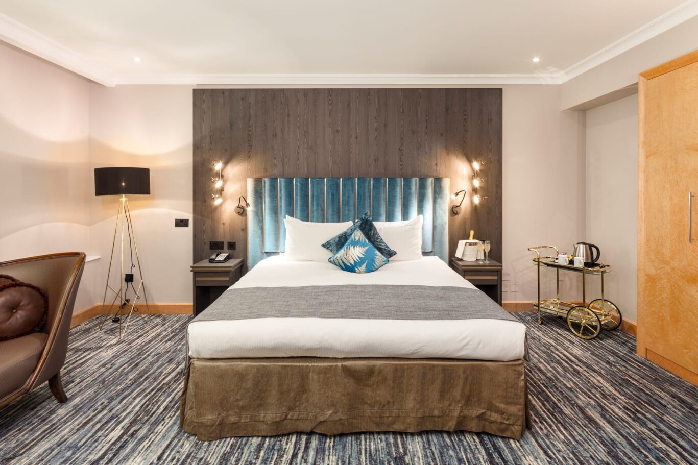 Large bedroom view with blue velvet headboard and tea trolley.
